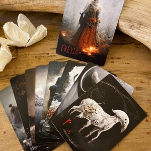 Puede incluir: Un juego de cartas de tarot con ilustraciones en blanco y negro. Las cartas presentan una variedad de im&aacute;genes, incluyendo una mujer con un vestido rojo, una oveja blanca con engranajes y una escena de bosque oscuro. Las cartas est&aacute;n dispuestas en forma de abanico sobre una superficie de madera.