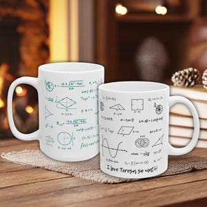 May include: Two white ceramic mugs featuring black and teal mathematical equations and formulas. One mug has the text "I love Teresa so much!" The mugs are displayed on a wooden surface.