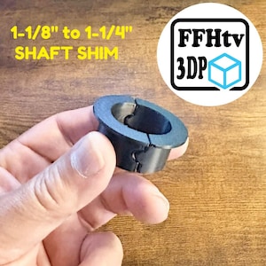 K&ouml;nnte beinhalten: Eine schwarze zylindrische Wellenpassfeder mit einem Flansch oben und einem vertikalen Schlitz an der Seite. Der Text 1-1/8" to 1-1/4" SHAFT SHIM ist in Gelb gedruckt, und ein Logo mit dem Text FFHtv 3DP und einem blauen W&uuml;rfelsymbol ist sichtbar.