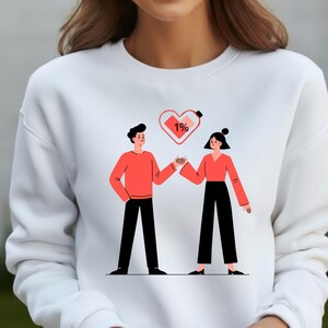 May include: White sweatshirt featuring a graphic of two figures holding hands, with a heart and battery icon above them. The heart shows 1% charge. The figures are wearing red tops and black pants.