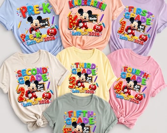 May include: A collection of seven colorful t-shirts in light blue, peach, lavender, cream, yellow, pink, and sage green. Each shirt features a graphic of Mickey Mouse, a red apple, pencils, and text indicating school grades from Pre-K to Fifth Grade.