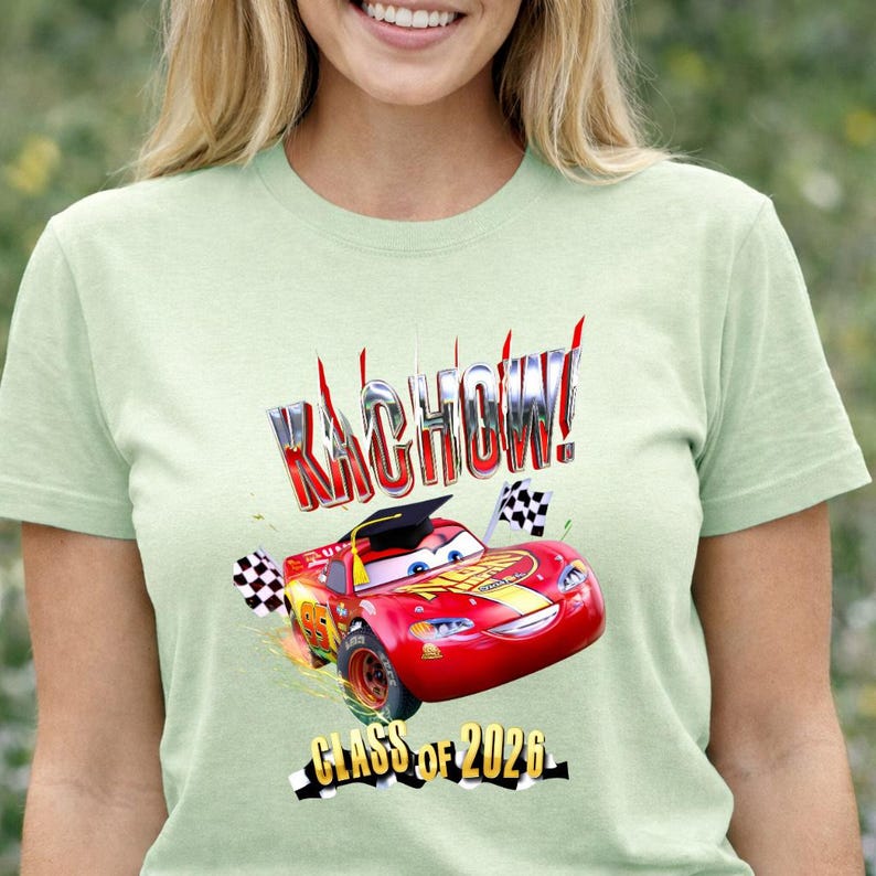 K&ouml;nnte beinhalten: Hellgr&uuml;nes T-Shirt mit einem roten Rennwagen-Motiv, dem Text "KACHOW!" und "CLASS OF 2026". Der Rennwagen hat eine Abschlusskappe und Zielflaggen. Das T-Shirt ist ein kurz&auml;rmeliges Rundhals-Shirt.
