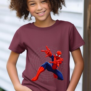 Puede incluir: Camiseta burdeos de manga corta con un dise&ntilde;o de Spider-Man. El superh&eacute;roe se muestra en una pose din&aacute;mica con las manos extendidas, sobre un fondo de telara&ntilde;a. El dise&ntilde;o presenta el traje rojo y azul de Spider-Man.