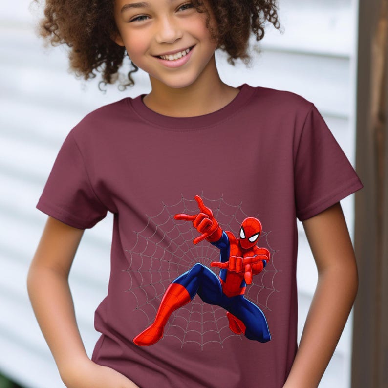 Puede incluir: Camiseta burdeos de manga corta con un dise&ntilde;o de Spider-Man. El superh&eacute;roe se muestra en una pose din&aacute;mica con las manos extendidas, sobre un fondo de telara&ntilde;a. El dise&ntilde;o presenta el traje rojo y azul de Spider-Man.