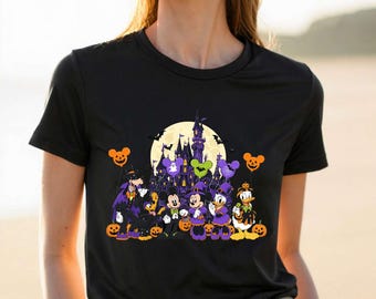May include: A black short-sleeved t-shirt featuring a graphic print of cartoon characters dressed in Halloween costumes. The design includes a large yellow moon, a dark castle, orange pumpkin balloons, and various jack-o'-lanterns on the ground.
