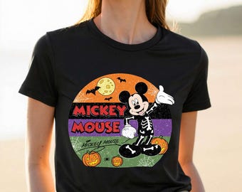 May include: A black t-shirt featuring a circular graphic with a yellow moon, bats, and spiderwebs. Mickey Mouse is depicted wearing a skeleton costume. The text reads MICKEY MOUSE in red and purple, with two orange jack-o'-lanterns at the bottom.