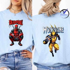 May include: Light blue t-shirts featuring comic book characters. One shirt displays Deadpool in a crouching pose with the text "DEADPOOL". The other shirt shows Wolverine with the text "WOLVERINE". Both shirts have a graphic print.