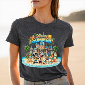 May include: A dark gray t-shirt featuring a colorful graphic of Disney characters Mickey Mouse, Minnie Mouse, Donald Duck, and Goofy on a beach in front of a castle. The text Disney SUMMER is printed in blue and yellow above the characters.