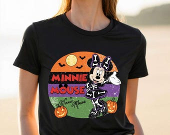 May include: A black short-sleeved t-shirt featuring a circular graphic with a yellow moon, black bats, and two orange pumpkins. The design includes the text MINNIE MOUSE and a cartoon character wearing a skeleton costume with a bow.