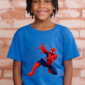 Puede incluir: Camiseta azul con un dise&ntilde;o de Spider-Man. La ilustraci&oacute;n muestra a Spider-Man en una pose din&aacute;mica con una telara&ntilde;a. El superh&eacute;roe est&aacute; en su traje rojo y azul, con los brazos extendidos.