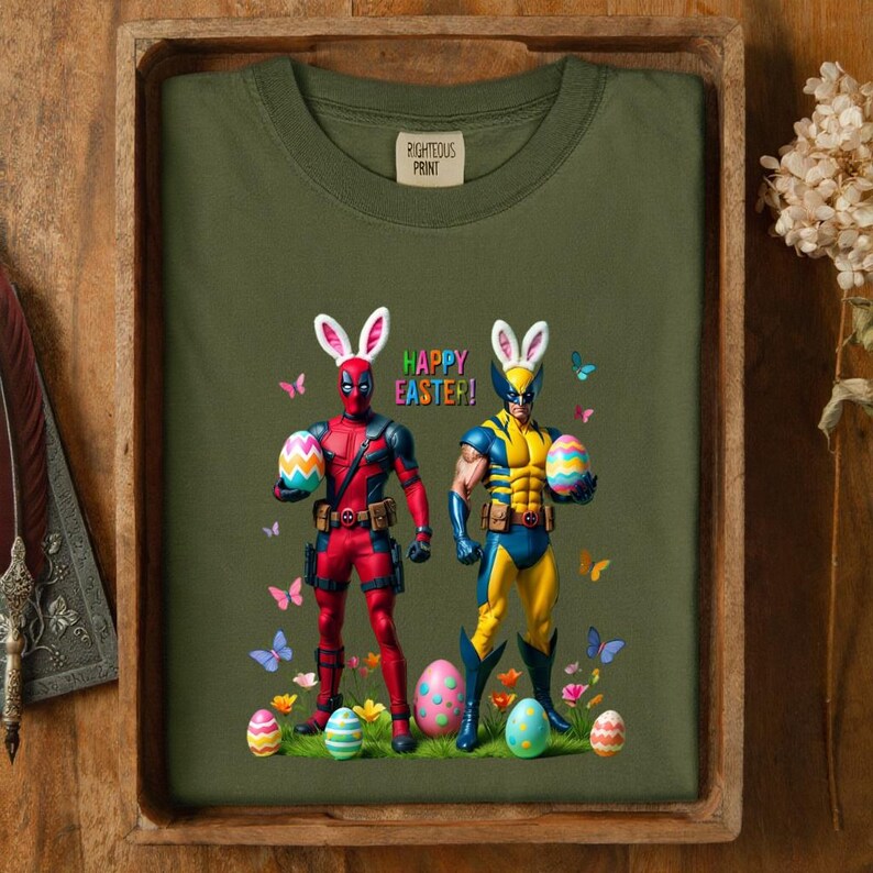 Puede incluir: Camiseta verde oliva con un gr&aacute;fico de Deadpool y Wolverine vestidos de conejitos de Pascua, sosteniendo huevos de Pascua. Las palabras "HAPPY EASTER!" est&aacute;n impresas encima de ellos. La camiseta tiene una etiqueta que dice "RIGHTEOUS PRINT".
