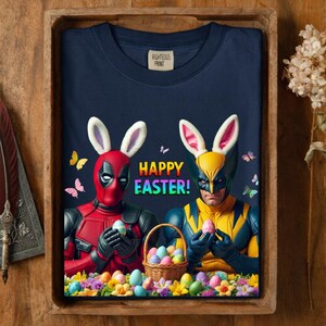 May include: Navy blue t-shirt with a colorful "Happy Easter!" graphic. The design features Deadpool and Wolverine wearing bunny ears and holding Easter eggs. A basket of eggs and colorful flowers are also included.