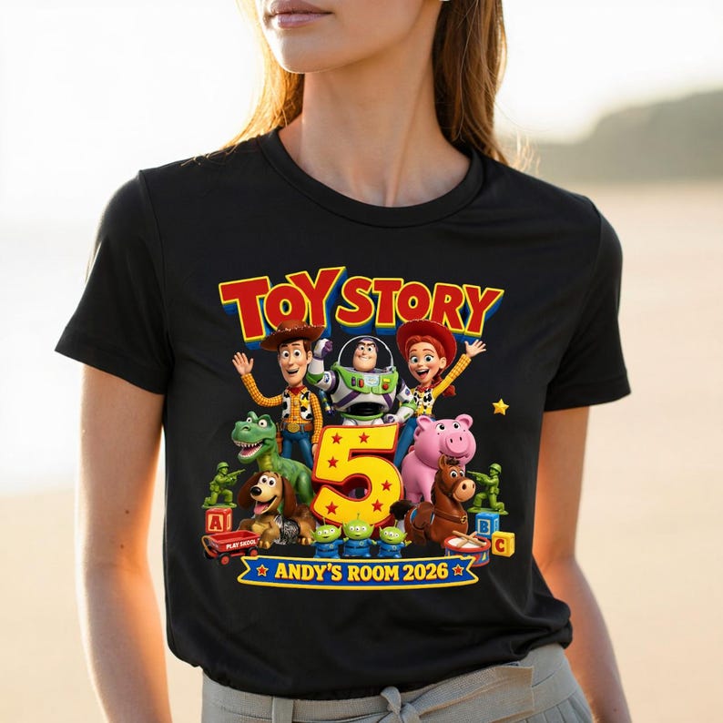 May include: A black t-shirt featuring a colorful Toy Story graphic with characters Woody, Buzz Lightyear, Jessie, Rex, Slinky Dog, Hamm, Bullseye, and green soldiers. A large yellow number 5 is centered, with the text TOY STORY and ANDY'S ROOM 2026.