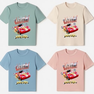 K&ouml;nnte beinhalten: Vier kurz&auml;rmelige T-Shirts in verschiedenen Farben: Salbeigr&uuml;n, Beige, Hellblau und Rosa. Jedes Shirt zeigt eine Grafik eines roten Rennwagens mit dem Text "KACHOW!" und "CLASS OF 2026".