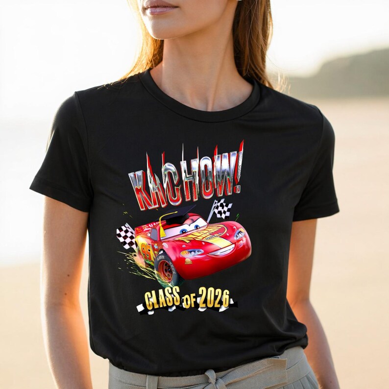 K&ouml;nnte beinhalten: Schwarzes T-Shirt mit einem roten Cartoon-Rennwagen-Design, dem Text "KACHOW!" in Silber und "CLASS OF 2026" in Wei&szlig;. Das Auto hat eine Abschlusskappe und karierte Flaggen.