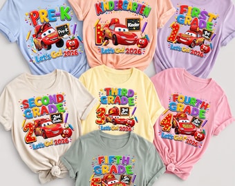 May include: Seven short-sleeve t-shirts in various pastel colors, each featuring a graphic of a red race car, a smiling apple, school supplies, and text ranging from Pre-K to Fifth Grade with the phrase Let's Go 2026 printed on the front.