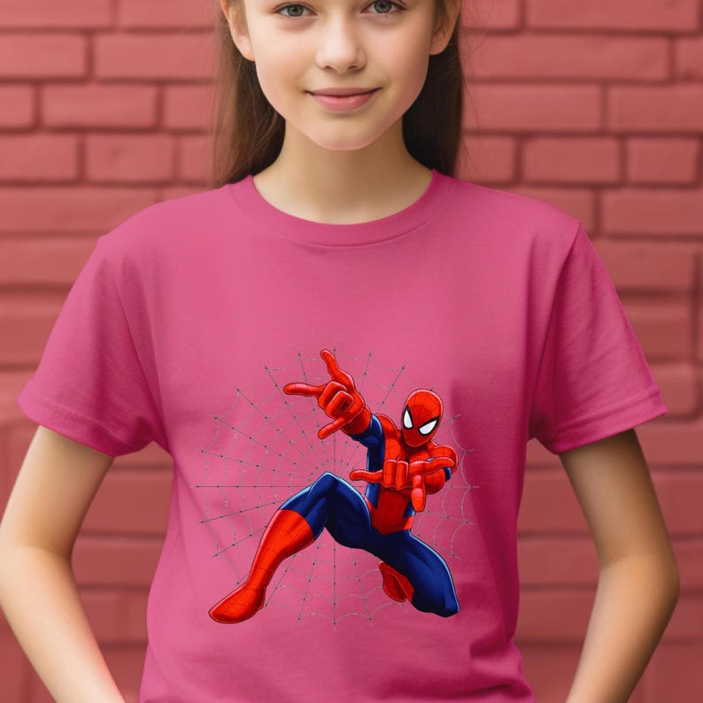 Puede incluir: Una camiseta rosa con un gr&aacute;fico de Spider-Man en una pose din&aacute;mica. El superh&eacute;roe est&aacute; representado en su cl&aacute;sico traje rojo y azul, con un dise&ntilde;o de telara&ntilde;a. La camiseta es de color rosa liso.
