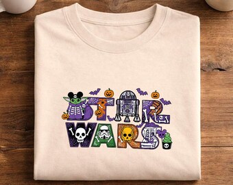 May include: A beige crew neck t-shirt featuring a graphic print that spells out STAR WARS. The letters are filled with Halloween-themed illustrations including skeletons, pumpkins, spider webs, bats, and Star Wars characters in skeleton costumes.