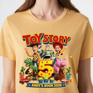 May include: A mustard yellow t-shirt featuring a Toy Story 5 graphic with characters Woody, Buzz Lightyear, Jessie, Rex, Slinky Dog, Hamm, Bullseye, and three aliens. The design includes a large number 5 and the text ANDY'S ROOM 2026.