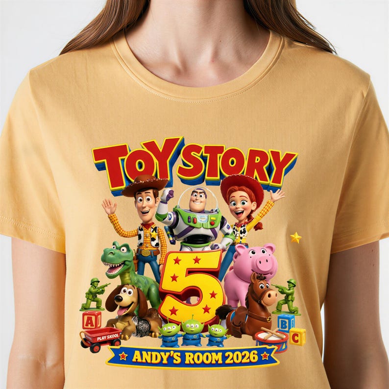 May include: A mustard yellow t-shirt featuring a Toy Story 5 graphic with characters Woody, Buzz Lightyear, Jessie, Rex, Slinky Dog, Hamm, Bullseye, and three aliens. The design includes a large number 5 and the text ANDY'S ROOM 2026.