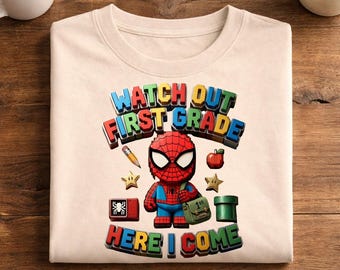 May include: A beige t-shirt featuring a graphic of a cartoon Spider-Man character wearing a green satchel. The text reads WATCH OUT FIRST GRADE HERE I COME. Surrounding elements include a pencil, an apple, two stars, a red block, and a green pipe.