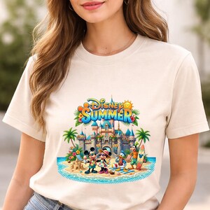 May include: A cream-colored t-shirt featuring a colorful graphic of Mickey Mouse, Minnie Mouse, Donald Duck, and Goofy on a beach in front of a castle. The text Disney Summer is printed in blue and yellow above the characters with palm trees.