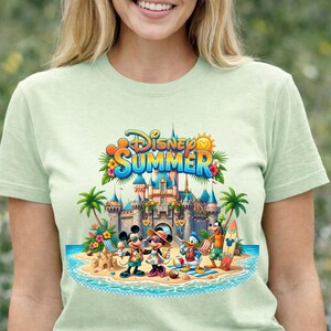 May include: A light green t-shirt featuring a graphic print of Disney characters Mickey Mouse, Minnie Mouse, Donald Duck, and Goofy on a beach in front of a castle. The text Disney SUMMER is printed in blue and orange above the castle illustration.
