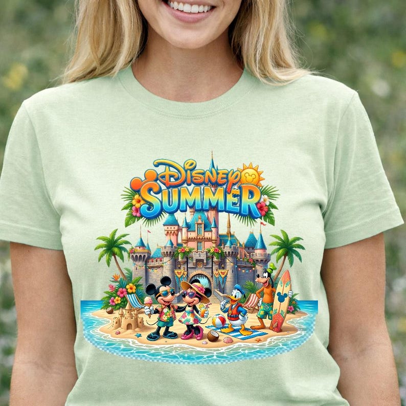May include: A light green t-shirt featuring a graphic print of Disney characters Mickey Mouse, Minnie Mouse, Donald Duck, and Goofy on a beach in front of a castle. The text Disney SUMMER is printed in blue and orange above the castle illustration.