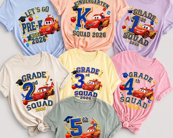 May include: A collection of seven short-sleeved t-shirts in various pastel colors, each featuring a red race car graphic, school supplies, and text indicating grade levels from Pre-K to 5th grade, all including the year 2026 in the design.