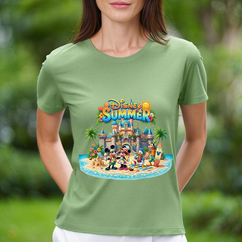 May include: A sage green short-sleeve t-shirt featuring a colorful graphic of Disney characters at a beach with a castle in the background. The text Disney SUMMER is printed in blue and yellow above the castle, with palm trees and sand.