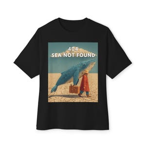 May include: Black t-shirt with a graphic featuring a blue whale, a person in a red coat, and the text "404 SEA NOT FOUND." The image has a surreal desert landscape background.