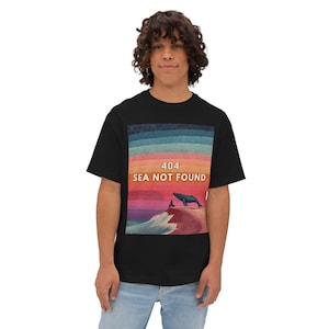 May include: Black t-shirt with a colorful graphic featuring a whale on a shore with the text "404 SEA NOT FOUND". The graphic has a sunset-like background with shades of blue, orange, and pink.
