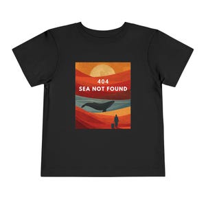 Könnte beinhalten: Schwarzes Kleinkind-T-Shirt mit einer Grafik einer Wal, einer Person und dem Text "404 SEA NOT FOUND" in Weiß. Die Grafik hat ein Farbschema mit Sonnenuntergang in Orange-, Rot- und Blautönen.