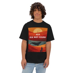 Może przedstawiać: Czarny t-shirt z nadrukiem zachodu słońca, wieloryba i napisem "404 SEA NOT FOUND". Grafika zawiera osobę z walizką. Koszulka wykonana jest z miękkiego materiału.