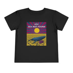 以下が含まれることがあります： 黒い幼児用Tシャツ。ひび割れた地面にクジラが描かれたグラフィック。グラフィックには、白と赤で「404 SEA NOT FOUND」というテキストが含まれています。