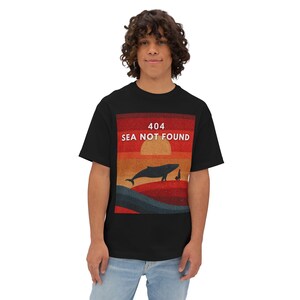 Może przedstawiać: Czarny t-shirt z nadrukiem zachodu słońca, sylwetką wieloryba i białym napisem "404 SEA NOT FOUND". Grafika zawiera wieloryba, małą postać i słońce. Koszulka jest noszona przez osobę.