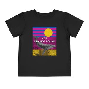 以下が含まれることがあります： 黒い幼児用Tシャツ。スーツケースに乗ったクジラのグラフィックと「404 SEA NOT FOUND」の文字。グラフィックには、黄色い太陽、ピンクと青のストライプ、ひび割れた地球の背景が含まれています。