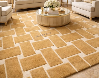 May include: A living room scene featuring a large, rectangular rug with a geometric pattern of golden-brown rectangles set against a cream background. The rug is the focal point, complemented by beige furniture and gold accents.