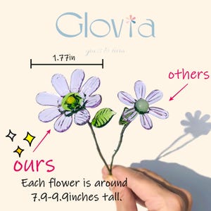 May include: Two glass flower stems with purple petals and green centers are held in a hand. The text says "Ours" and "Each flower is around 7.9-9.9 inches tall." The logo "Glovia" is at the top.