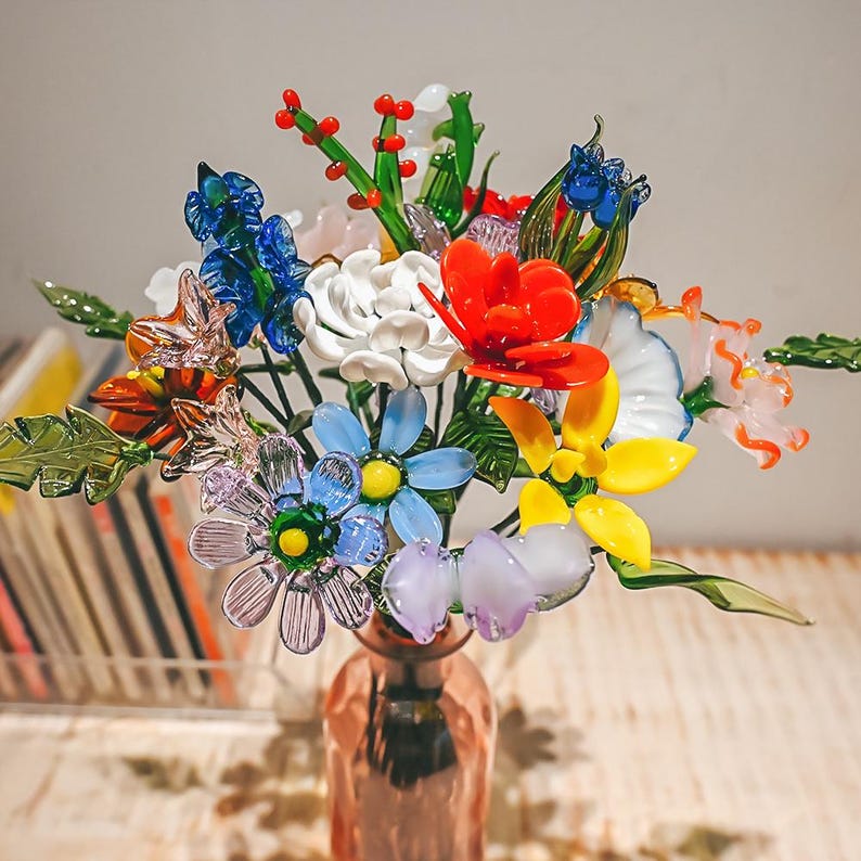 May include: A colorful glass flower bouquet in a copper-colored vase. The arrangement includes red, blue, yellow, and white flowers, with green leaves and stems. The glass flowers are intricately detailed and appear delicate.