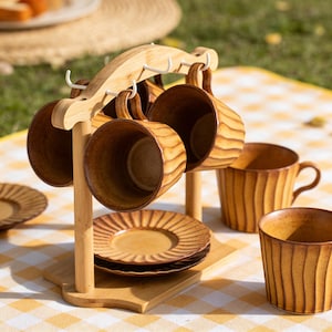 May include: A wooden mug tree holds six brown ceramic mugs with matching saucers. The mugs and saucers have a textured, ridged design. The mug tree is made of light-colored wood and has white hooks for hanging the mugs.
