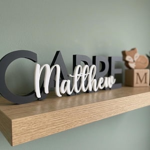 May include: A decorative sign featuring the black block letters spelling CARPE and the white cursive script name Matthew layered in front. The sign is displayed alongside a small wooden block with the letter M and a fox figurine.