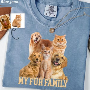 May include: A blue jean colored t-shirt featuring a graphic print of two golden retriever dogs and two orange tabby cats. The text "MY FUR FAMILY" is printed in yellow below the animals. The shirt has a Comfort Colors label showing size S.