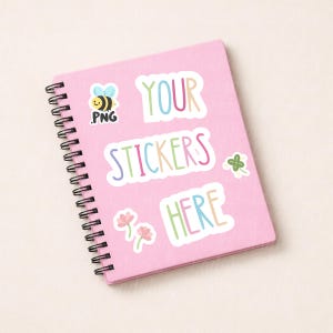 May include: A pink spiral-bound notebook with the text "YOUR STICKERS HERE" in colorful letters. The notebook is decorated with sticker designs, including a bee, a four-leaf clover, and pink flowers.