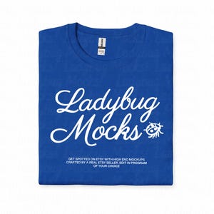 Op de afbeelding: Een gevouwen koningsblauw t-shirt met de woorden "Ladybug Mocks" in witte letters. Een kleine lieveheersbeestje-afbeelding staat naast het woord "Mocks". De tekst "GET SPOTTED ON ETSY WITH HIGH END MOCKUPS CRAFTED BY A REAL ETSY SELLER, EDIT IN PROGRAM OF YOUR CHOICE" staat eronder.