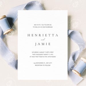 Pode incluir: Um convite de casamento branco com texto preto, com os nomes Henrietta e Jamie e os detalhes da cerim&oacute;nia. Uma fita azul clara e bobinas de madeira envolvem o convite.