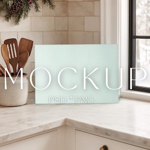 May include: A light blue rectangular mockup with the word "MOCKUP" in white, and the text "PSD + PNG" below it. The mockup is on a white countertop, with wooden kitchen utensils in a ceramic pot to the left. A window is visible on the right.
