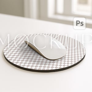 May include: A white wireless computer mouse rests on a round mousepad with a checkered pattern in shades of gray and white. The mousepad has a black border. The image includes the text "MOCKUP" in a light gray font.