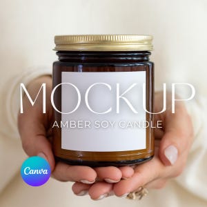 May include: An amber-colored soy candle in a glass jar with a gold lid. The candle has a white label with the word "MOCKUP" and "AMBER SOY CANDLE" printed on it. The candle is held in two hands.