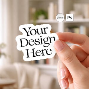 Puede incluir: Una pegatina blanca con borde negro y el texto "Your Design Here". La pegatina está sujeta por una mano, con un fondo borroso de una habitación con una estantería.